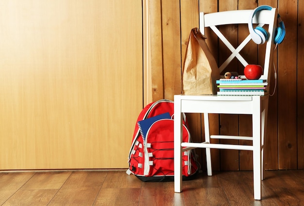 Plecak z przyborami szkolnymi na krześle na drewnianym tle