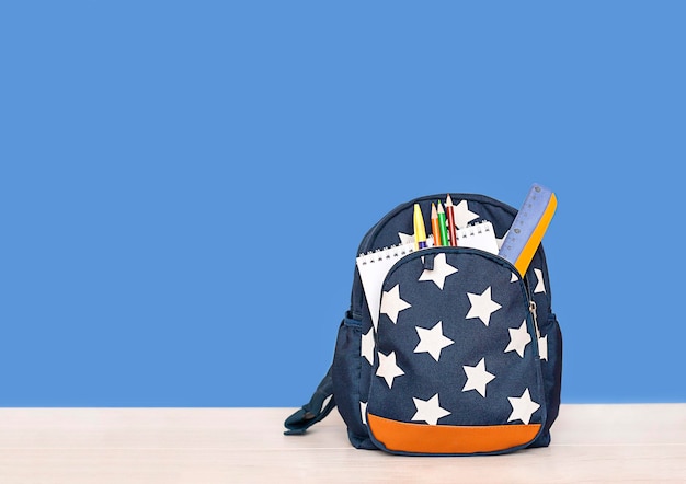 plecak z przyborami szkolnymi stoi na stole na niebieskim tle