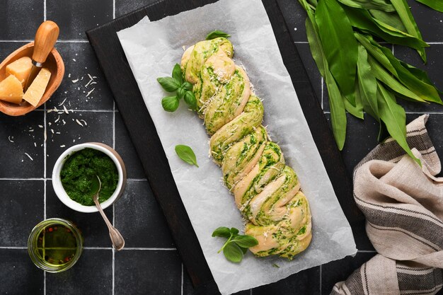 Pleciona brioche z pesto z dzikiego czosnku Domowy surowy lub niegotowany świeży chleb z pesto z dzikiego czosnku na drewnianej desce na starym czarnym tle stołu Włoski chleb Kopiowanie miejsca Widok z góry