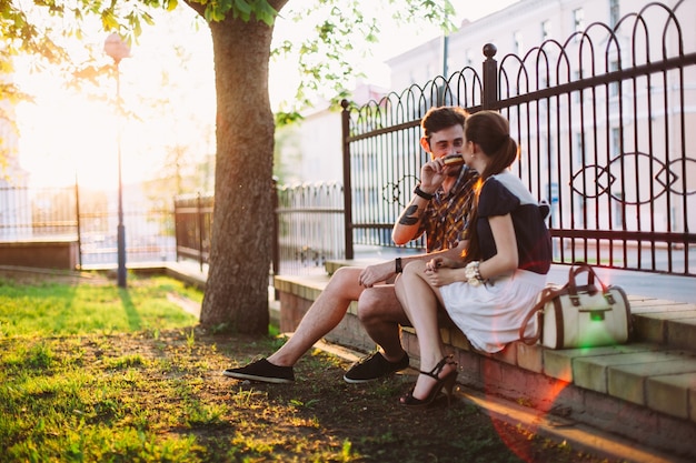 Plenerowy lato portret piękna para ma zabawę w parku wpólnie. Przystojny mężczyzna daje czekoladowy pączek jego dziewczynie