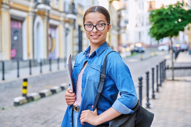 Plenerowy portret uśmiechniętej nastoletniej studentki patrzącej na kamerę w mieście