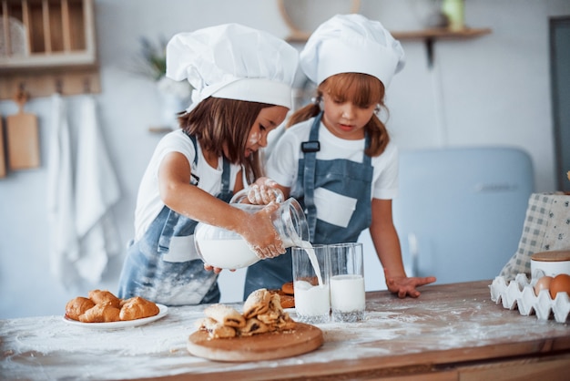 Pliki cookie są gotowe. Rodzinne dzieci w białym mundurze szefa kuchni przygotowuje jedzenie w kuchni.