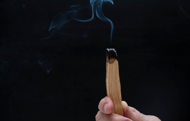 Płonąca laska palo santo w rękach na czarnym tle