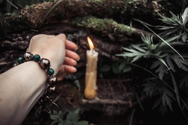 Płonące świece i kobieca ręka z bransoletką na ciemnym naturalnym tle pogańskie wiccan słowiańskie tradycje Czary ezoteryczny duchowy rytuał na mabon halloween samhain jesienny festiwal równonocy