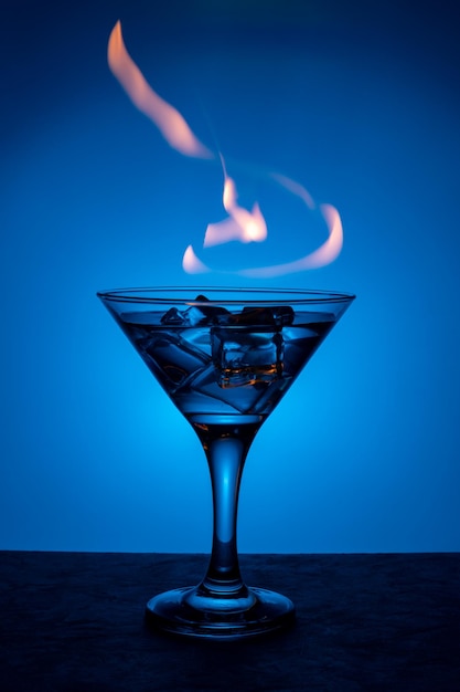 Płonący napój alkoholowy z kostkami lodu na niebieskim tle gradientu Płonący koktajl na stole w barze