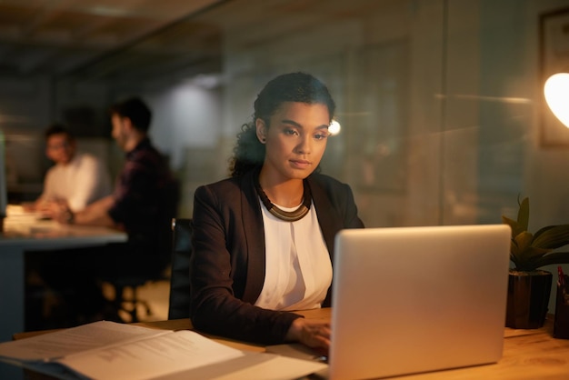Płonący olej o północy Ujęcie młodej bizneswoman korzystającej z laptopa podczas pracy w godzinach nadliczbowych w biurze