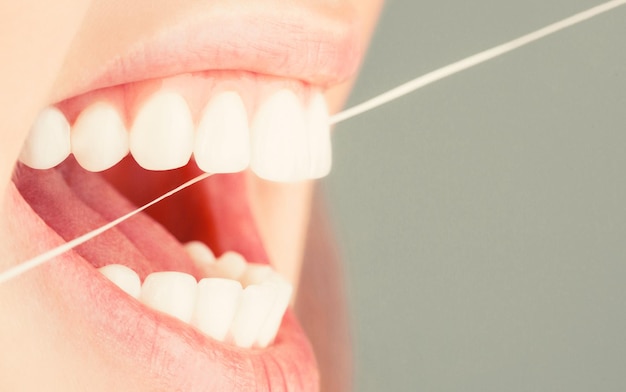 Płukanie zębów kobieta nitkowanie zębów Nić dentystyczna Dbanie o zęby Koncepcja zdrowych zębów Nitkowanie zębów Higiena jamy ustnej i opieka zdrowotna Uśmiechnięte kobiety używają nici dentystycznej Białe zdrowe zęby