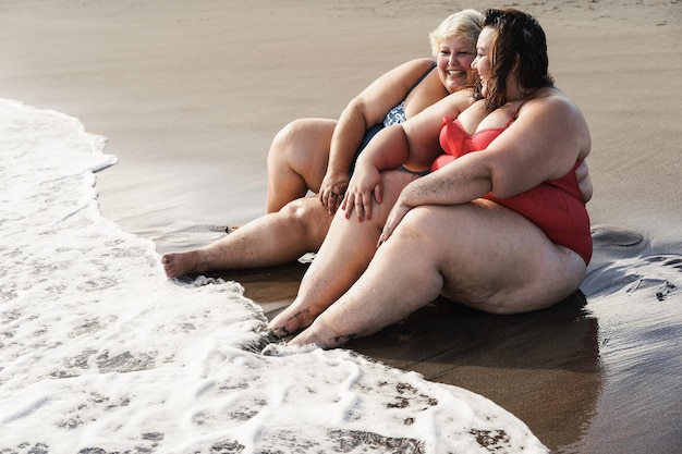 Plus Size Kobiety Siedzące Na Plaży I Bawiące Się Podczas Letnich Wakacji - Skoncentruj Się Na Prawej Twarzy