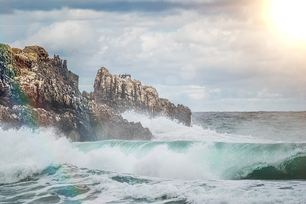 Plusk wody oceanu na skalnej plaży z pięknym słonecznym niebem i chmurami. Fala morska rozpryskiwania się na kamieniu na brzegu morza na zimę. Fale morskie uderzają o kamień na plaży?