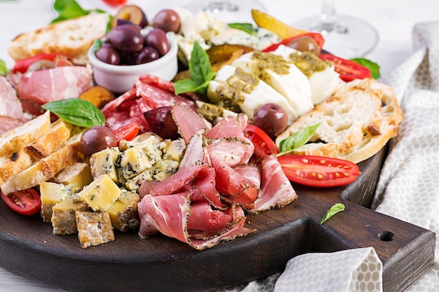 Płytka antipasto z szynką, prosciutto, salami, mozzarellą z niebieskim serem, pesto i oliwkami na drewnianym tle