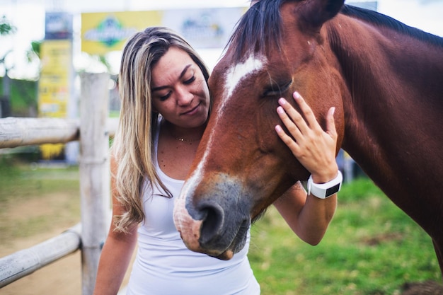 Płytkie skupienie młodej latynoskiej kobiety pieszczącej brązowego konia na farmie pod słońcem