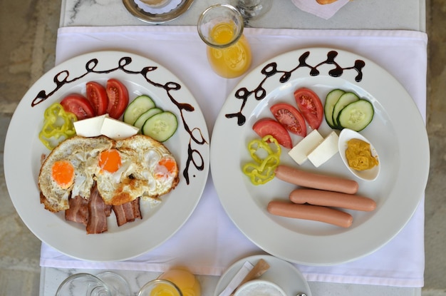 Zdjęcie płyty z podawanym śniadaniem - smażone jajka, bekon, hot-dogi i świeże warzywa