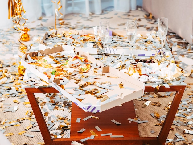 Po imprezowym chaosie Bałagan w pokoju Podłoga i stół z pizzą i kieliszkami do szampana pokryte konfetti Resztki uroczystości