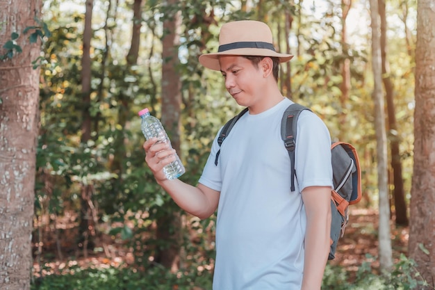 Po lesie spaceruje turysta mężczyzna niosący butelkę wody w torebce i aparat fotograficzny