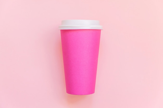 Po prostu płasko leżał różowy papierowy kubek do kawy na różowym pastelowym kolorowym modnym tle. Pojemnik na napoje na wynos