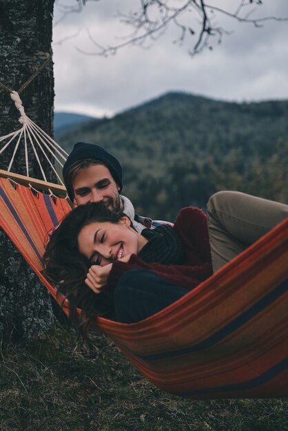 Po prostu zakochany. Piękna młoda para obejmując się i uśmiechając leżąc w hamaku pod drzewem