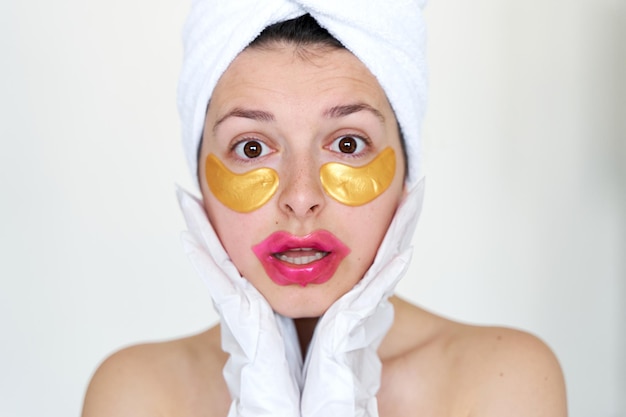 Po prysznicu dziewczyna owinięta ręcznikiem stosuje plastry kosmetyczne na skórę pod oczami usta i rękawiczki do nawilżenia dłoni i stóp Trendy kosmetyczne w pielęgnacji ciała w domu