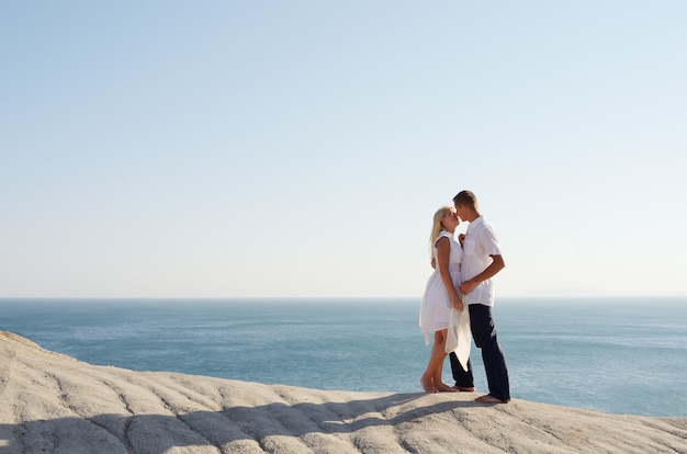 Pocałunek młodej pary ubranej na biało blisko morza