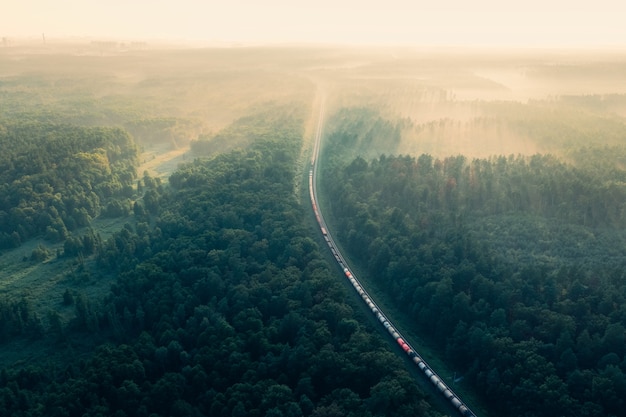Pociąg w letnim lesie rano o wschodzie mgły widok z lotu ptaka poruszającego się pociągu towarowego w lesie
