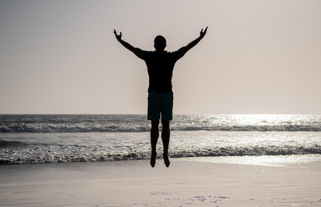 Poczuj wolność młody i wolny sportowiec skaczący w oceanie poranna aktywność treningowa zdrowy mężczyzna sylwetka podniósł ręce na plaży energiczne lato