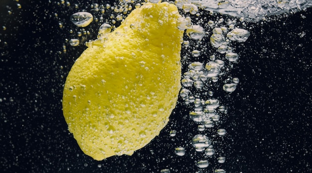 Zdjęcie pod wodą świeżo wyciśnięta słodzona lemoniada, której plasterek surowej cytryny wpada do wody sodowej na ciemnoniebieskim lub czarnym tle zbliżenie lemoniady lub zimnego koktajlu cytrynowego highball zimny napój orzeźwiający