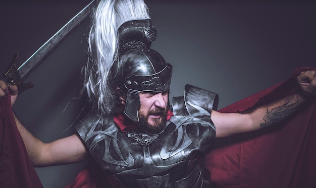 Zdjęcie podbój rzymski gladiator, zapaśnik i wojownik rzymu w hełmie i czerwonym płaszczu, nosi żelazny miecz, brodę i długie włosy.