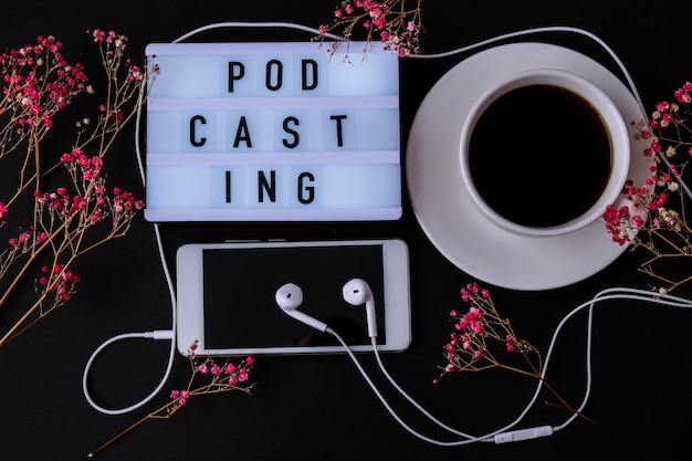 Podcasting napis słuchawki telefon komórkowy suche różowe kwiaty dekoracja miejsce pracy czarna kawa