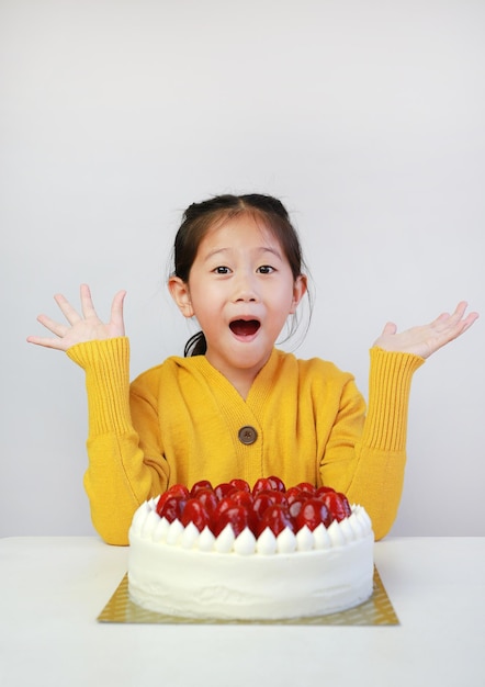 Podekscytowana azjatycka dziewczynka z tortem truskawkowym Dzieciak z tortem urodzinowym na stole