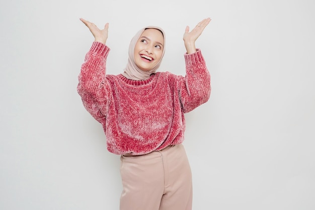 Podekscytowana azjatycka kobieta ubrana w różowy sweter i hidżab, wskazująca na miejsce kopiowania na niej, odizolowana białym tłem