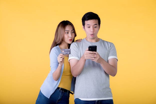 Podekscytowana Azjatycka Para Trzymająca Kartę Kredytową I Smartfona, Która Czuje Się Podekscytowana, Patrząc Na Telefon Komórkowy Odizolowany Na Kolorowym Tle