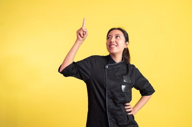 Podekscytowana azjatycka szefowa kuchni z palcem skierowanym w górę na odosobnionym tle