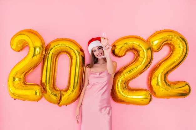 Podekscytowana dziewczyna podnosi kieliszek szampana w santas hat złote balony na nowy rok koncepcja