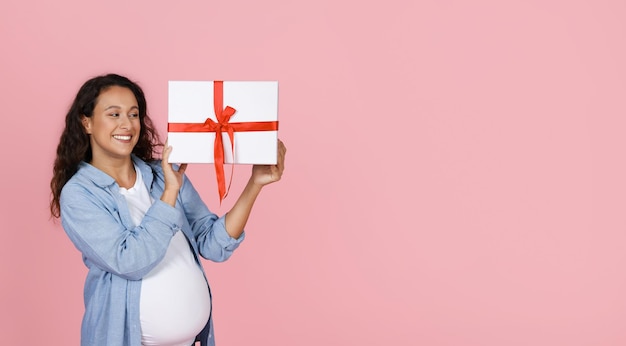 Podekscytowana kobieta w ciąży trzymająca pudełko z prezentami.