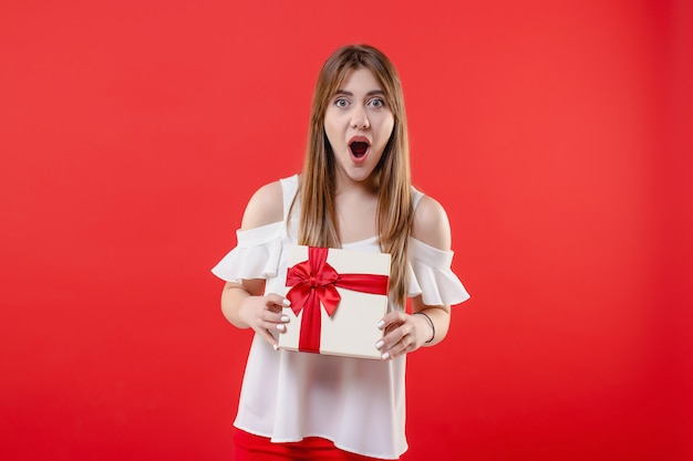 Podekscytowana kobieta z pudełko na sobie białą bluzkę na białym tle na czerwonej ścianie