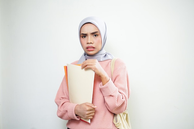 Podekscytowana młoda azjatycka muzułmańska studentka w różowym swetrze z torbą trzymającą książkę