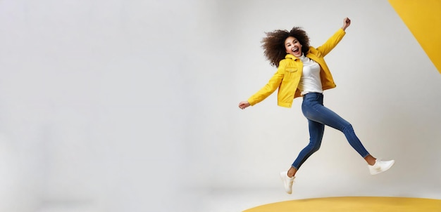 Podekscytowana młoda dziewczyna świętuje sukces i skacze wysoko na żółtym białym tle