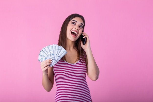 Podekscytowana młoda kobieta trzyma banknoty pieniądze za pomocą telefonu komórkowego