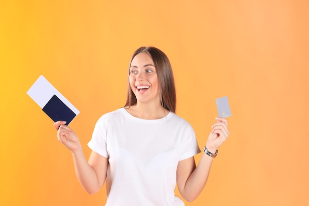 Podekscytowana młoda kobieta turystyczna stojąca na białym tle na żółtym tle, trzymając paszport z biletami, plastikową kartą kredytową.