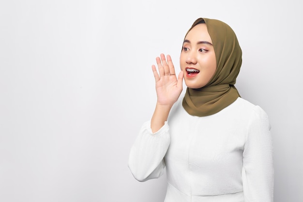 Podekscytowana młoda piękna azjatycka muzułmanka 20 lat nosząca hidżab krzyczy i krzyczy wiadomości rękami blisko ust odizolowana na białym tle Koncepcja religijnego stylu życia ludzi