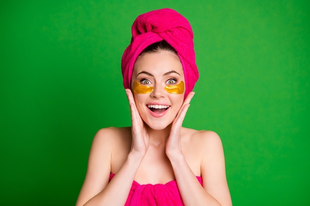 Podekscytowana pani używa plastrów pod oczami spojrzenie lustro ramiona dotyka kości policzkowych ręczniki ciało głowa izolowany zielony kolor tła