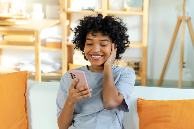 Podekscytowana, szczęśliwa, młoda, czarna Afroamerykanka trzymająca telefon komórkowy, śmiejąca się, czująca radość z dostania tłumu