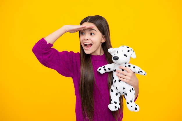 Podekscytowana twarz Nastoletnia dziewczynka dziecko w stroju casualowym trzymająca pluszową zabawkę na białym tle na żółtym tle szczęśliwe dzieciństwo Zdumiony wyraz wesoły i zadowolony