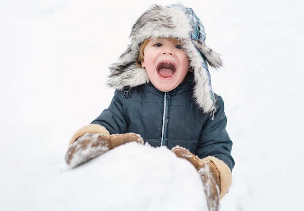 Podekscytowane dziecko bawiące się ze śniegiem słodkie dziecko w czapce zimowej bawiące się śnieżką w winter park w ...