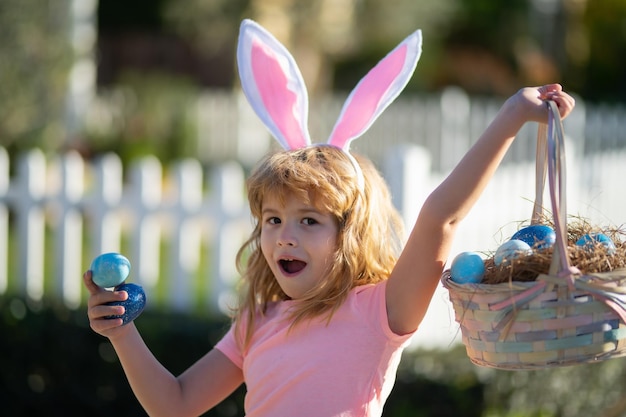 Podekscytowane dziecko z koszykiem wielkanocnym chłopiec polujący na pisanki dzieciak z jajkami wielkanocnymi i uszami królika