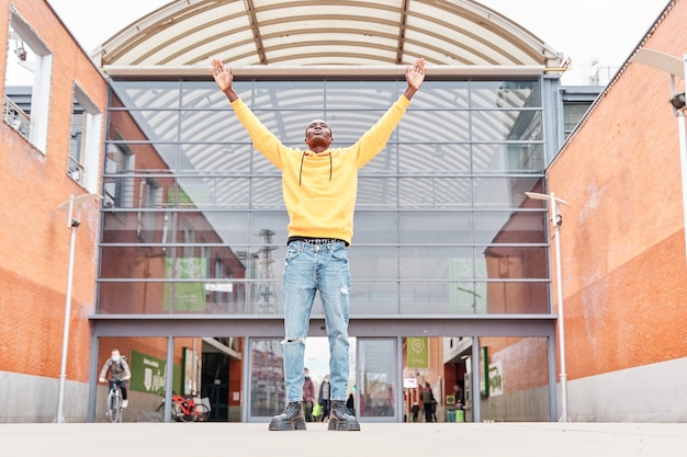 Podekscytowany Afroamerykanin świętuje sukces, podnosząc ręce w mieście z budynkami w tle