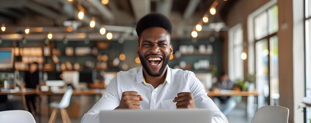 Podekscytowany Afroamerykanin świętuje sukces pracując z laptopem w biurze Koncepcja Świętowanie sukcesu Afroamerykański Człowiek Środowisko biurowe Laptop Zadowolenie z pracy