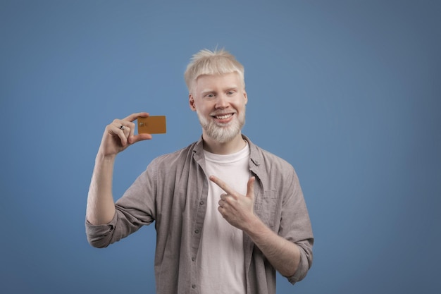 Podekscytowany albinos, który wskazuje na kartę bankową w dłoni i uśmiecha się do kamery, polecając bankowi koniec