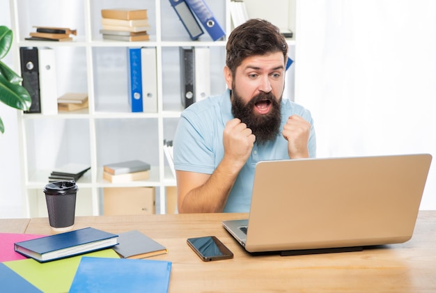Podekscytowany biznesmen robi pięści patrząc w laptop na biurku oczekiwanie