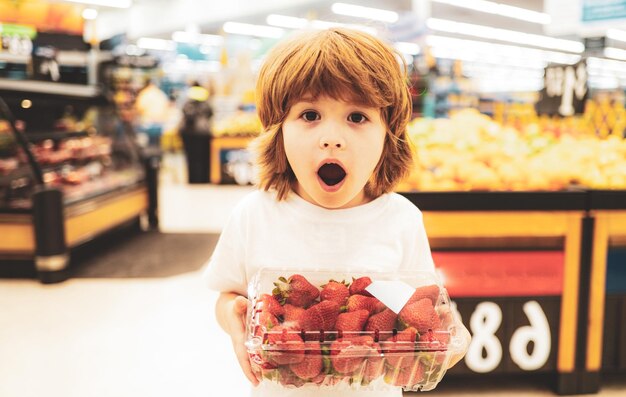 Podekscytowany chłopiec w supermarkecie kupuje warzywa truskawki zdrowe jedzenie dla dzieci śmieszne zakupy