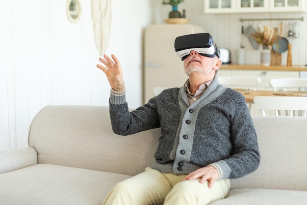 Podekscytowany dojrzały starszy mężczyzna noszący używając wirtualnej rzeczywistości metaverse VR okulary słuchawki w domu dziadka